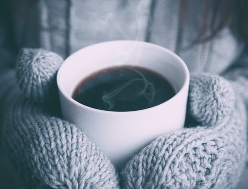 hands with knitted gloves hold white cup with hot coffee